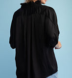 Woman wearing a black blouse and denim shorts against a light blue background