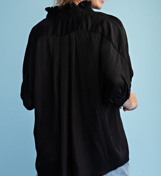 Woman wearing a black blouse and denim shorts against a light blue background