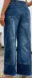 Person wearing blue wide-leg jeans standing on a concrete surface with a white wall in the background.