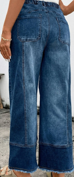 Person wearing blue wide-leg jeans standing on a concrete surface with a white wall in the background.