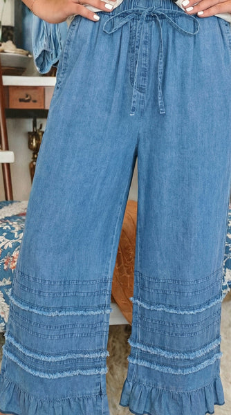 Person wearing blue denim pants with ruffled bottom hem in a casual setting.
